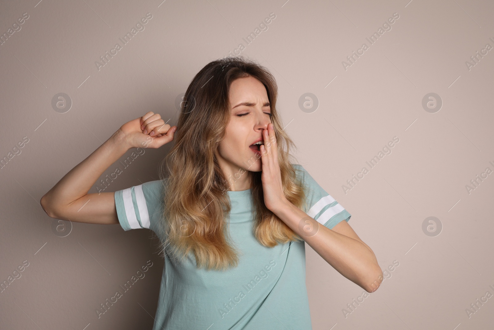 Photo of Young tired woman yawning on beige background