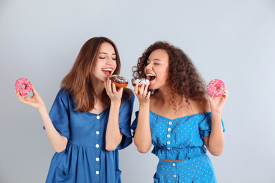 Beautiful young women with donuts on light grey background