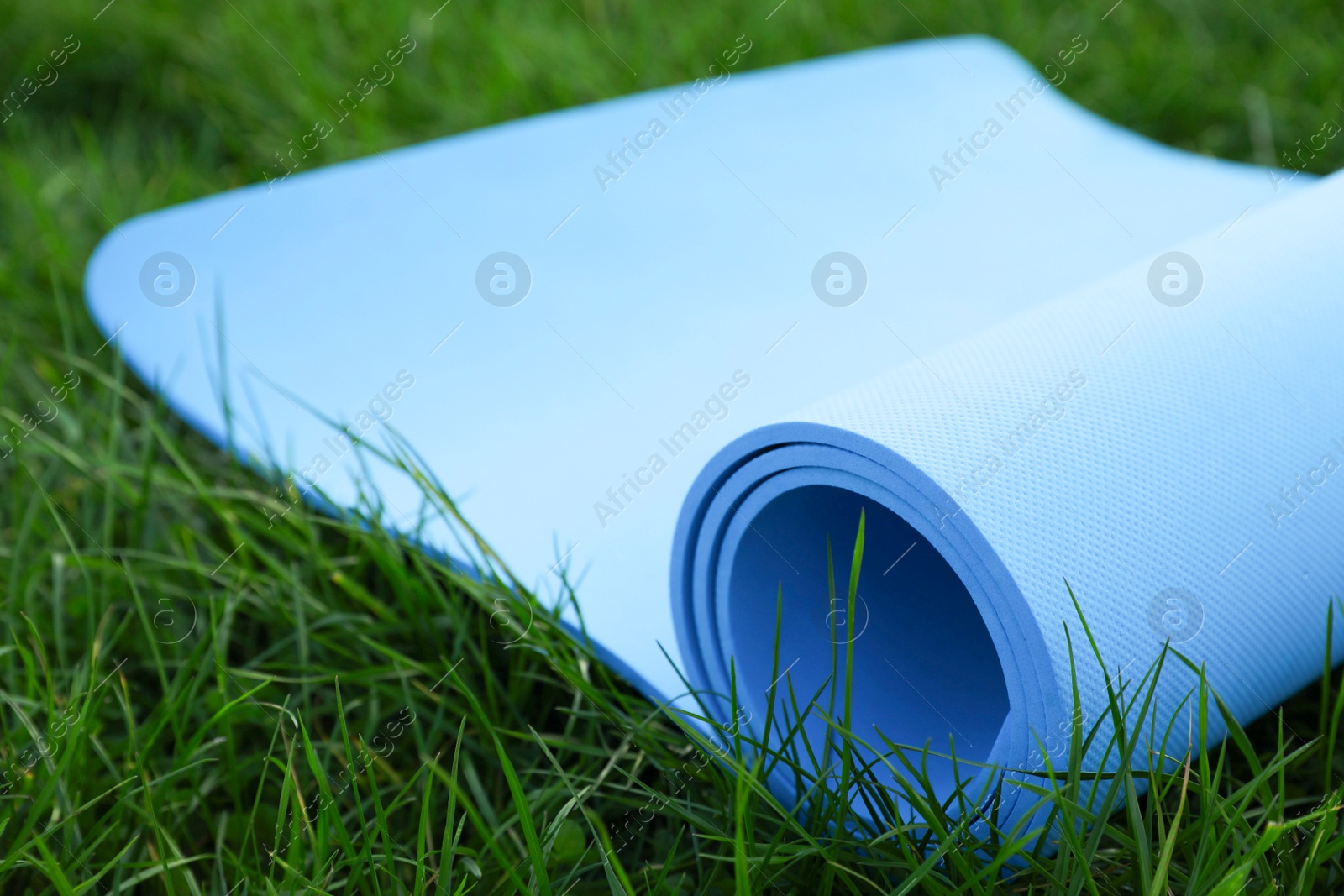 Photo of Blue karemat or fitness mat in fresh green grass outdoors, closeup