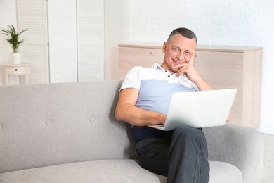 Photo of Mature man with laptop sitting on sofa at home