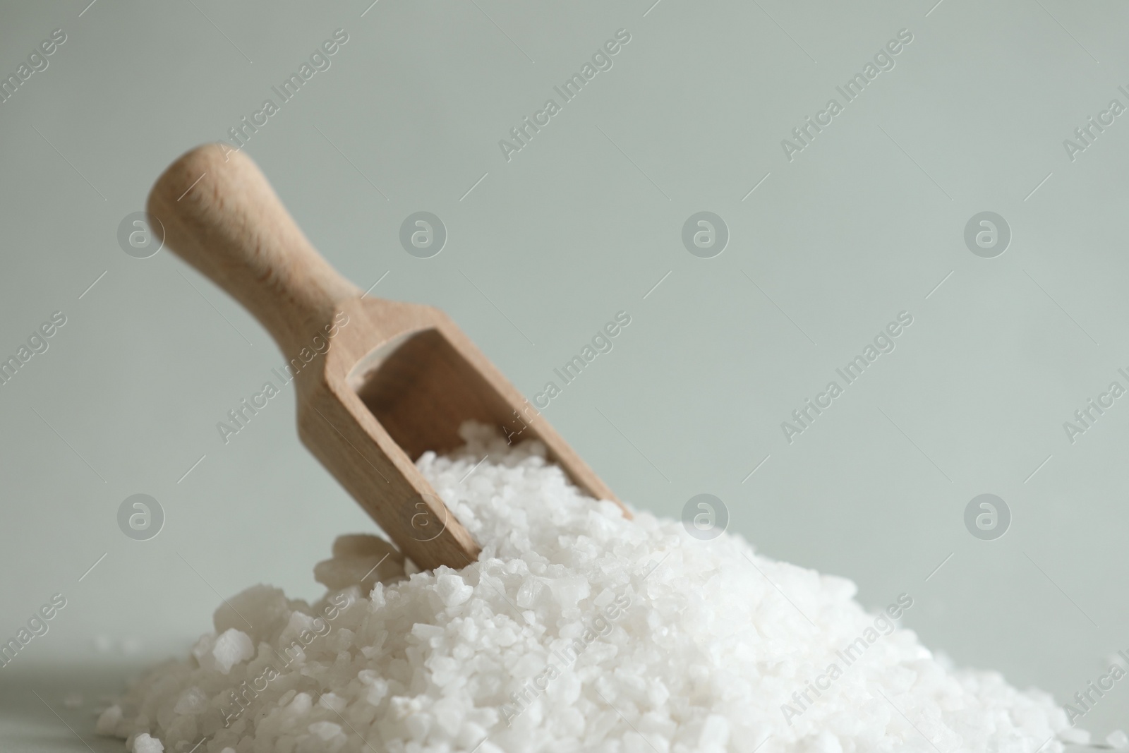 Photo of Organic salt and wooden scoop on light grey background, closeup. Space for text