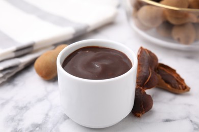 Photo of Bowl of tamarind sauce and fresh pods on white marble table