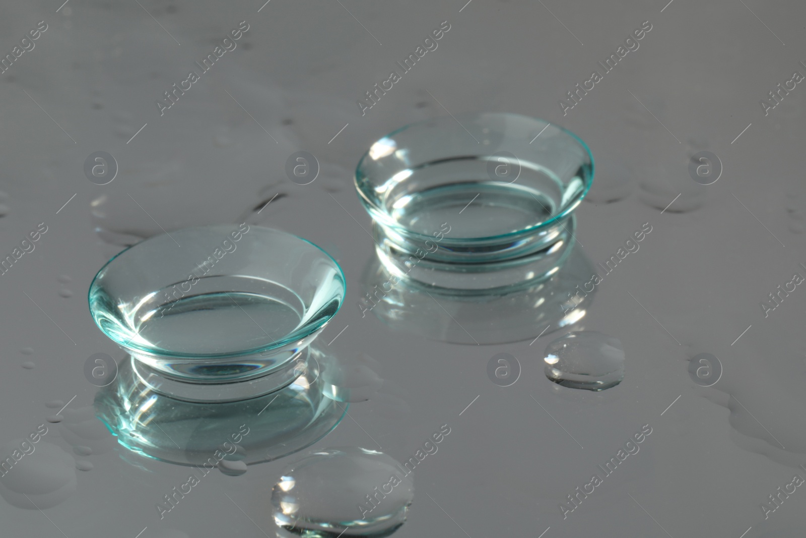 Photo of Pair of contact lenses on wet grey reflective surface