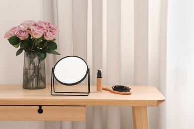 Photo of Mirror, foundation, brush and vase with pink roses on wooden dressing table in makeup room, space for text