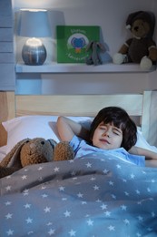 Cute little boy with toy bunny sleeping in bed at home