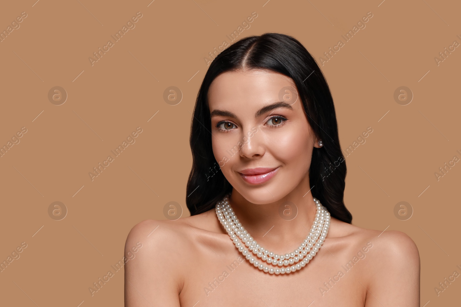 Photo of Young woman wearing elegant pearl jewelry on brown background, space for text