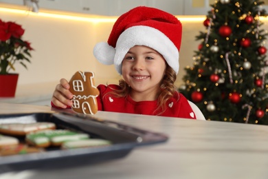 Photo of Cute little girl with freshly baked Christmas gingerbread cookie at table indoors