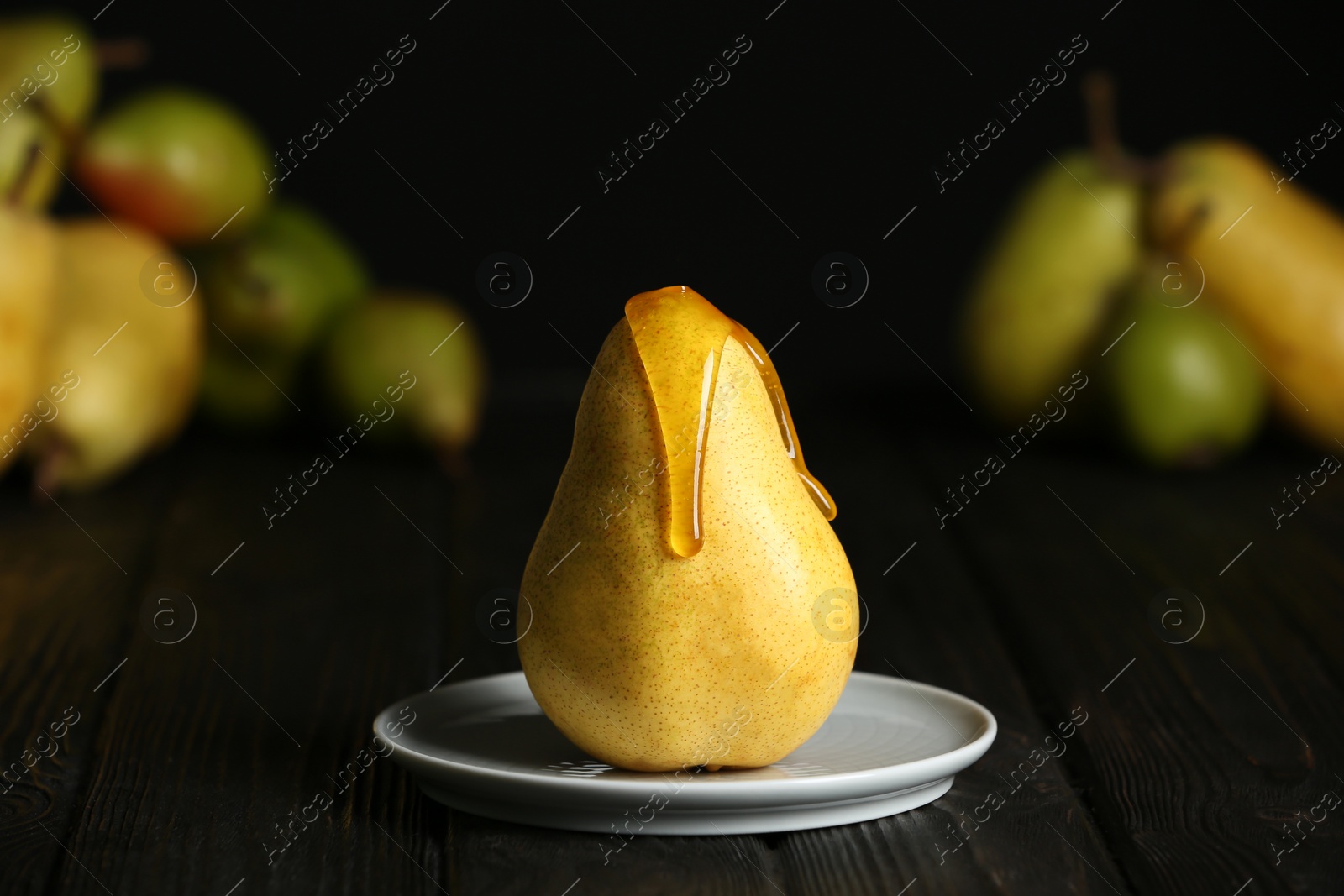 Photo of Pouring sweet syrup onto fresh ripe pear on table against blurred background