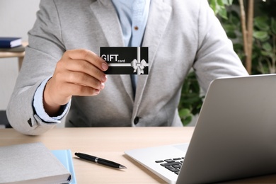 Photo of Man with gift card and laptop at table indoors, closeup