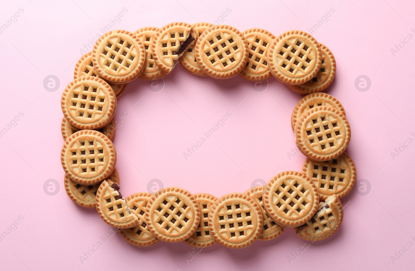Photo of Frame of tasty sandwich cookies with cream on pink background, flat lay. Space for text