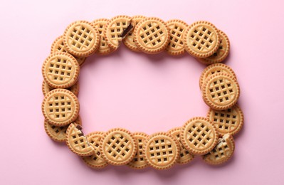 Photo of Frame of tasty sandwich cookies with cream on pink background, flat lay. Space for text