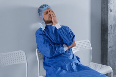 Photo of Exhausted doctor sitting on chair near grey wall indoors