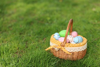 Photo of Easter celebration. Painted eggs in wicker basket on green grass, space for text