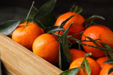 Photo of Fresh ripe tangerines and leaves in wooden crate, closeup
