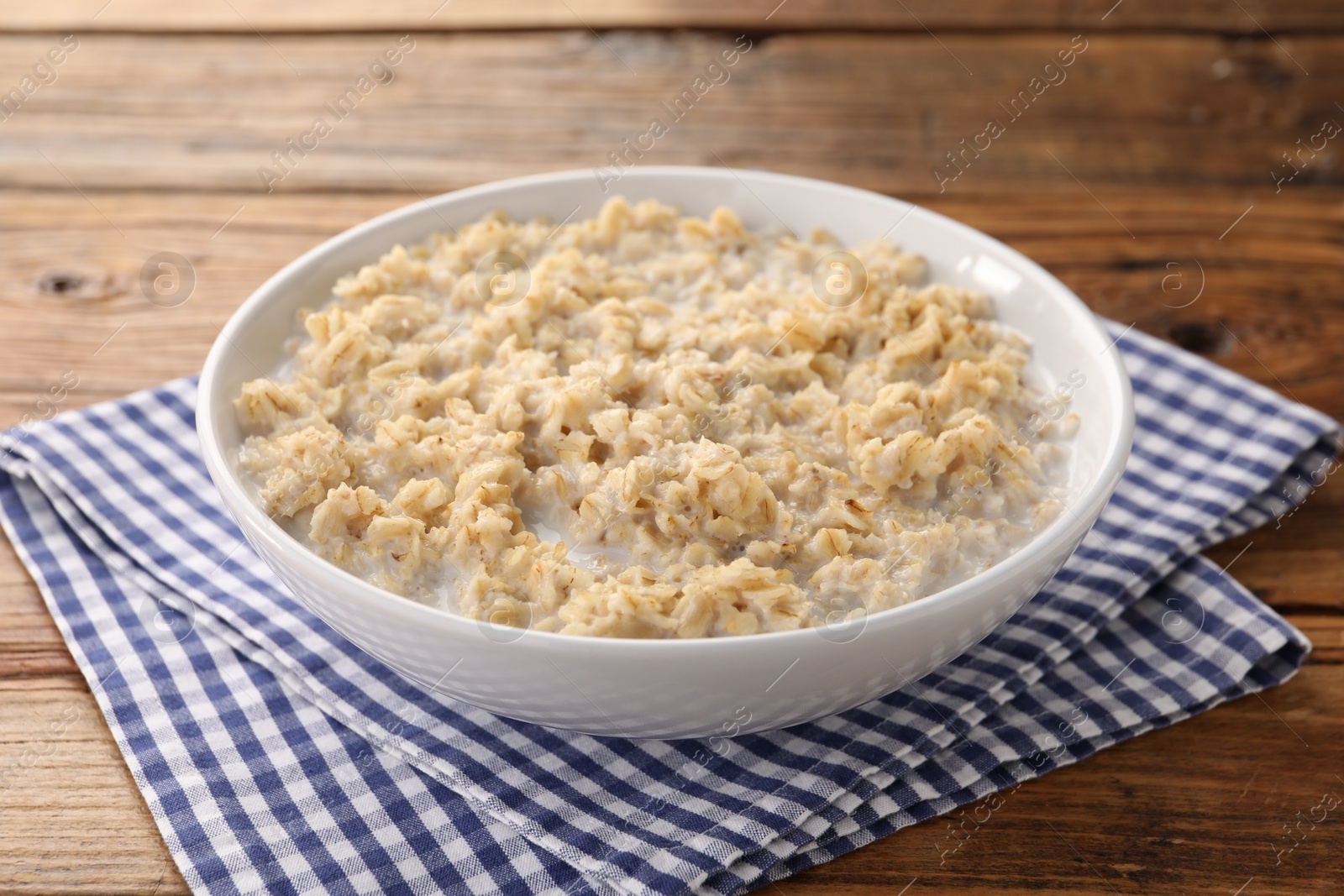 Photo of Tasty boiled oatmeal in bowl on wooden table