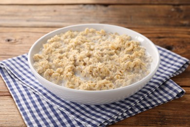 Photo of Tasty boiled oatmeal in bowl on wooden table