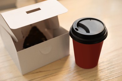 Photo of Hot coffee in takeaway cup and box with dessert on wooden table indoors