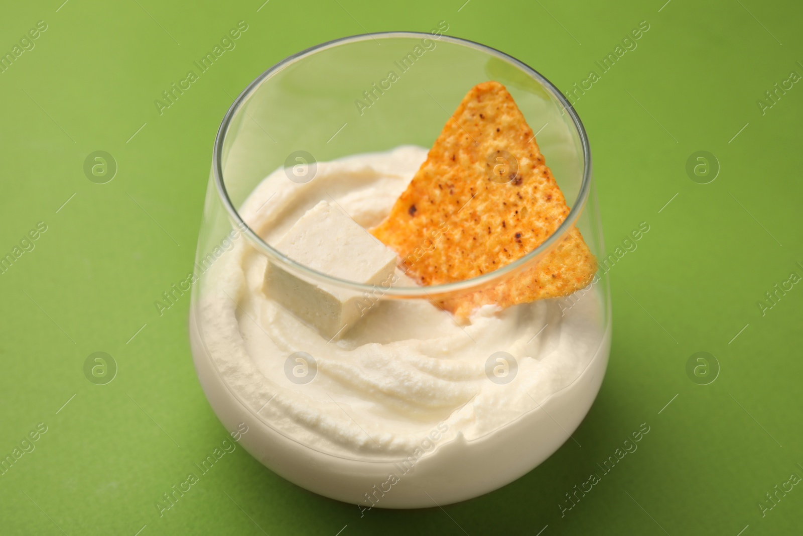 Photo of Delicious tofu sauce served with nachos chip on green background, closeup