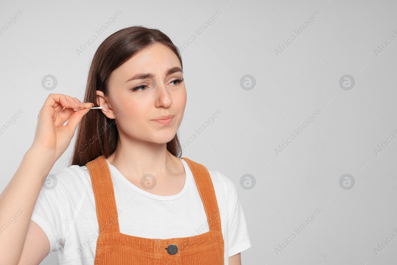 Photo of Young woman cleaning ear with cotton swab on light grey background. Space for text