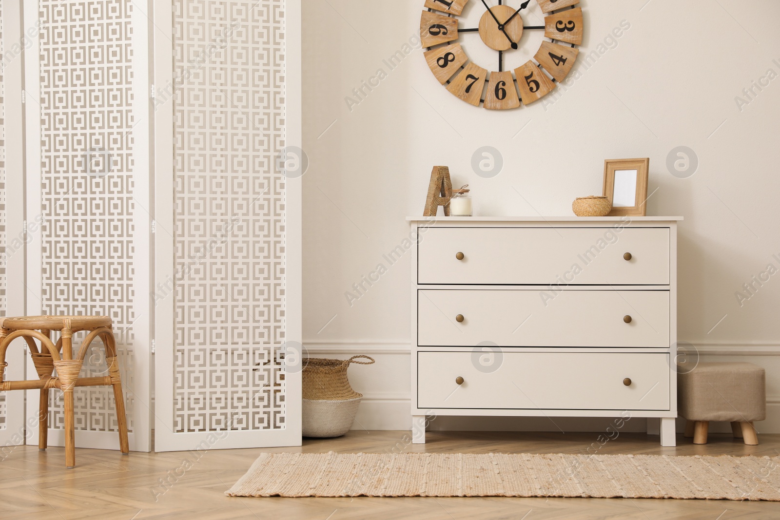 Photo of Stylish room with wooden folding screen and chest of drawers near white wall. Interior design