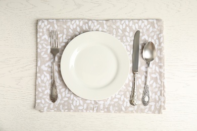 Photo of Empty plate, cutlery and napkin on white wooden table, flat lay