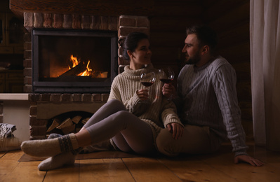 Photo of Lovely couple with glasses of wine near fireplace at home. Winter vacation