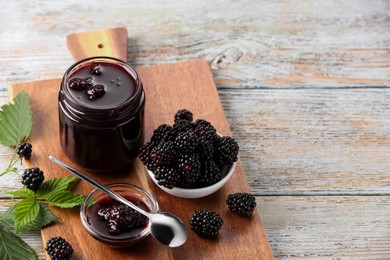 Photo of Fresh ripe blackberries, tasty jam and leaves on rustic wooden table. Space for text