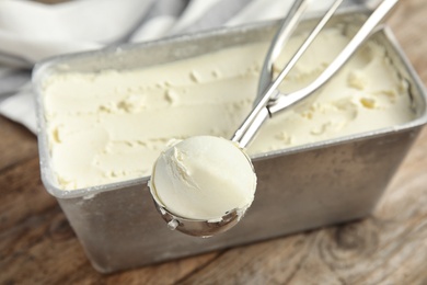 Photo of Container and scoop with delicious vanilla ice cream on wooden table, closeup