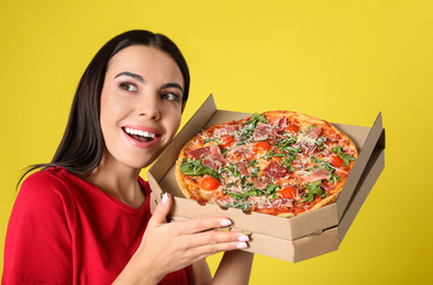 Beautiful woman with tasty pizza on yellow background