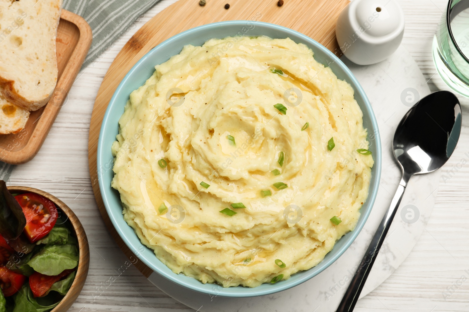 Photo of Bowl of tasty mashed potatoes with onion served on white wooden table, flat lay