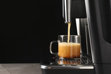 Photo of Modern espresso machine pouring coffee into glass cup on grey table against black background. Space for text