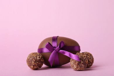 Tasty chocolate egg with purple bow and candies on pink background. Space for text