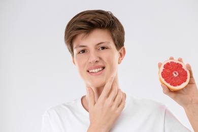 Photo of Teenage boy with acne problem holding grapefruit on light background. Skin allergy