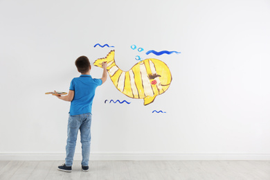 Little child drawing yellow whale on white wall indoors