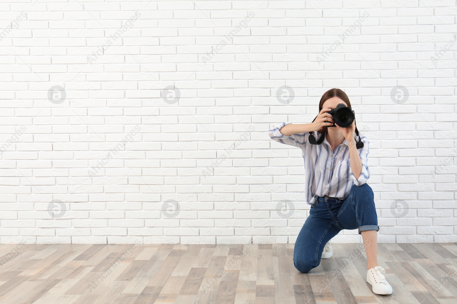 Photo of Professional photographer taking picture near white brick wall. Space for text