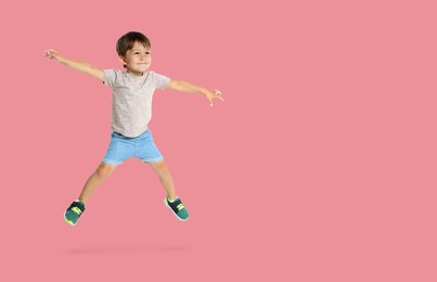 Happy boy jumping on pink background, space for text