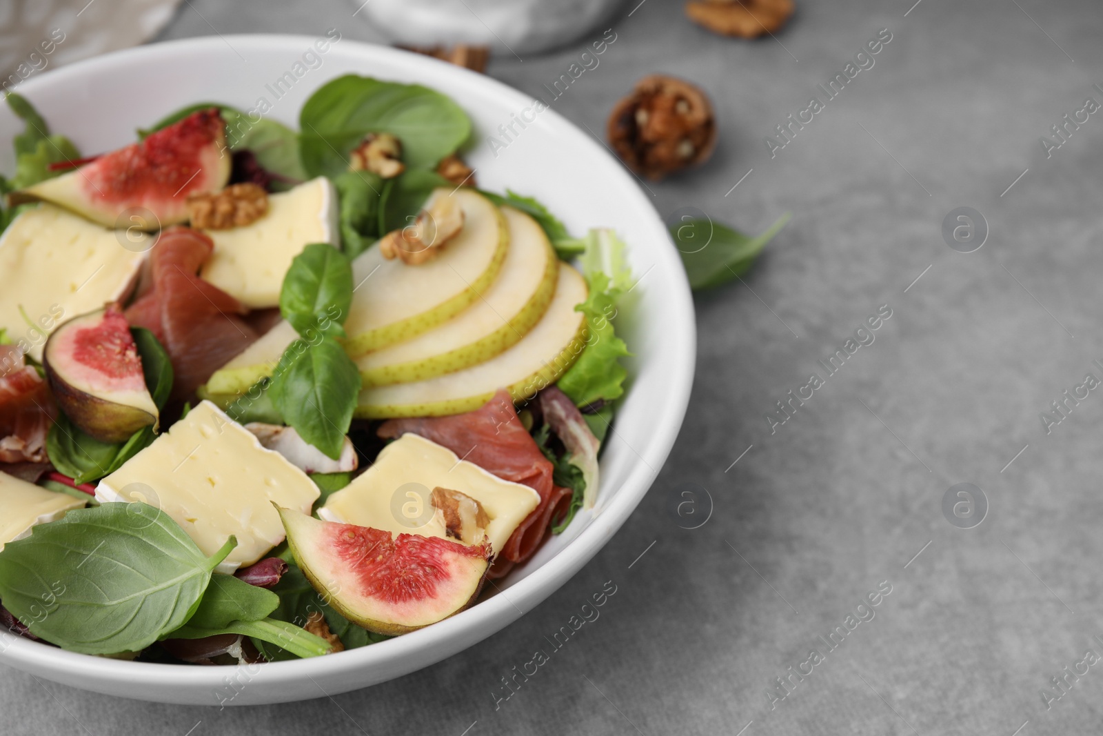 Photo of Tasty salad with brie cheese, prosciutto, pear and figs on grey table, closeup. Space for text