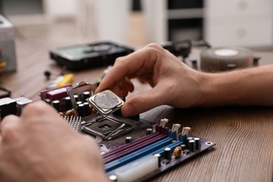 Photo of Male technician repairing motherboard at table, closeup