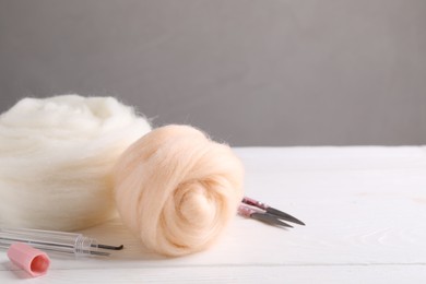 Felting wool and tools on white wooden table. Space for text