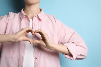 Woman making heart with hands on light blue background, closeup