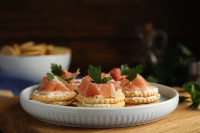 Photo of Delicious crackers with cream cheese, prosciutto and parsley on table