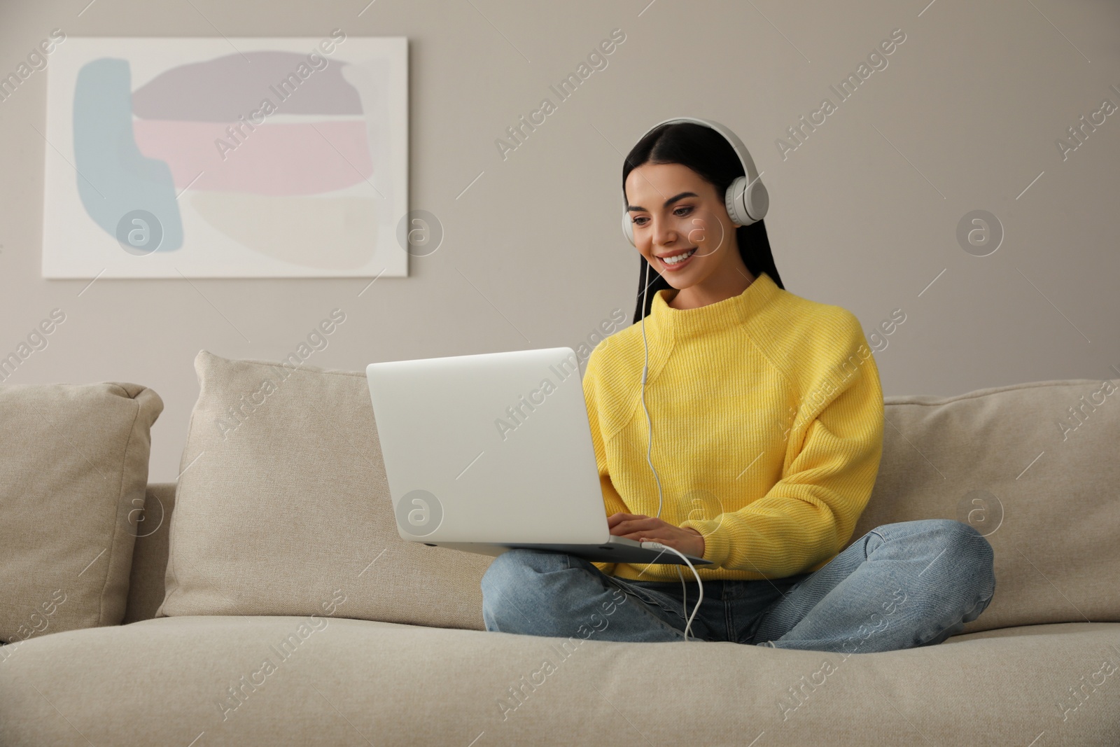 Photo of Woman with laptop and headphones sitting on sofa at home