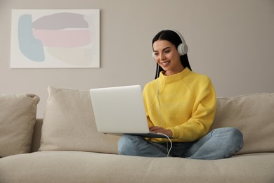 Woman with laptop and headphones sitting on sofa at home