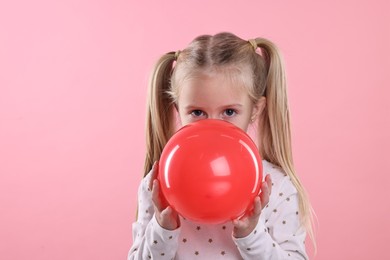 Photo of Cute little girl inflating red balloon on pink background