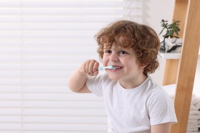 Cute little boy brushing his teeth with plastic toothbrush indoors, space for text