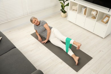 Photo of Senior woman doing exercise with fitness elastic band on mat at home