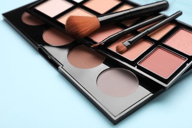 Photo of Colorful contouring palettes with brushes on light blue background, closeup. Professional cosmetic product