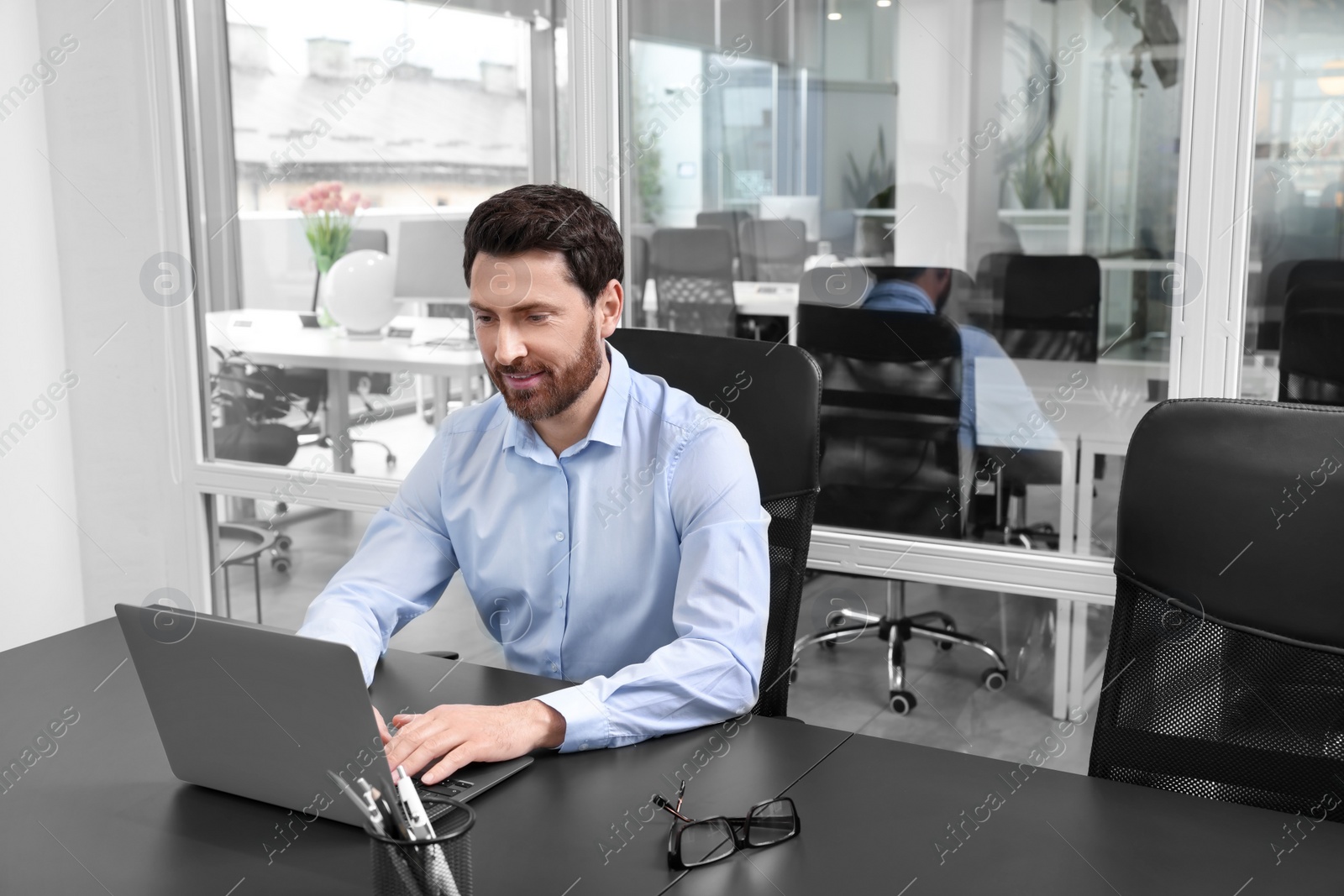 Photo of Man working on laptop at black desk in office. Space for text