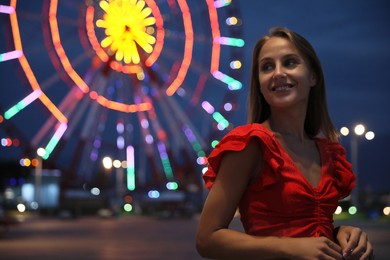 Photo of Beautiful young woman against glowing Ferris wheel in amusement park, space for text