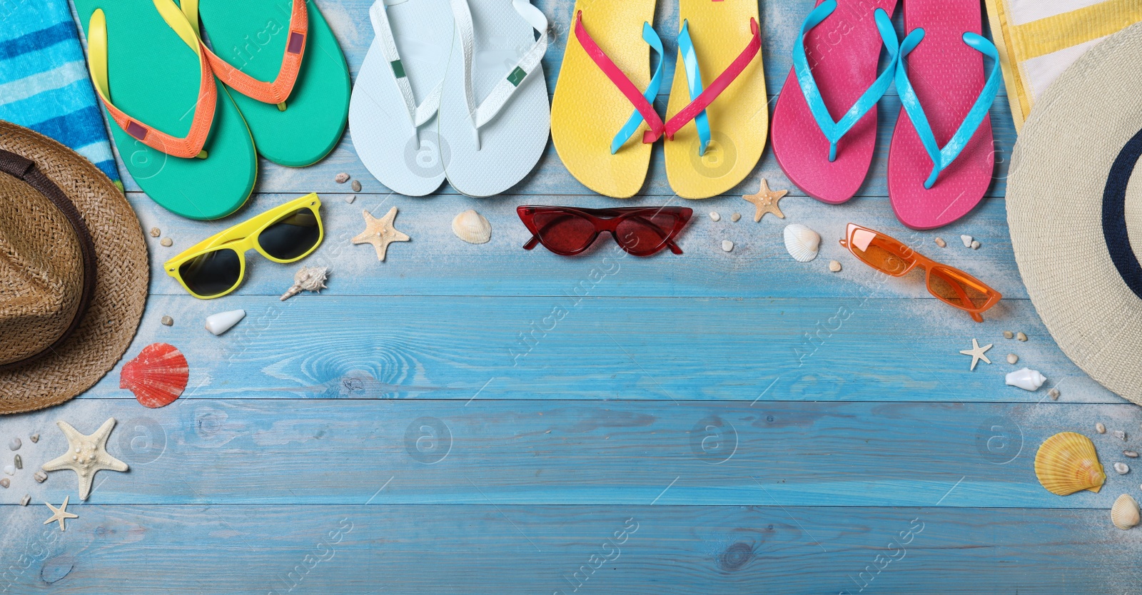 Photo of Many different flip flops and beach objects on light blue wooden background, flat lay. Space for text